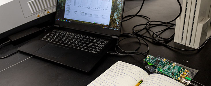 Student workplace with a laptop, circuit board, and written notes