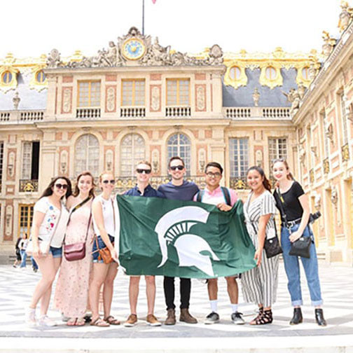 MSU Engineering student group holding a Spartan Flag in front of a building at CEA Paris Center