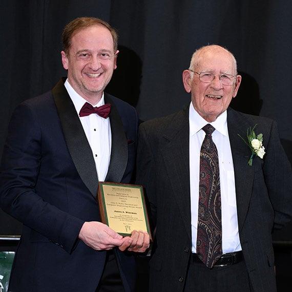 James Wineman holding his award next to John Papapolymerou