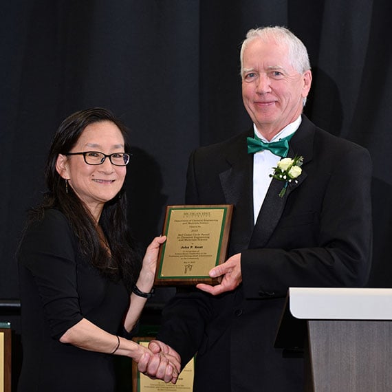 John Kent holding his award and shaking hands with Christina Chan