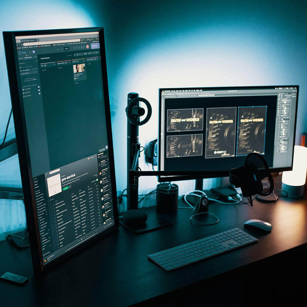 Dual-monitor desk setup with keyboard, mouse, headphones, and speakers in blue lighting